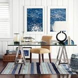 coastal theme home office with glass transparent desk and shiplap walling, ocean wall art and striped carpet